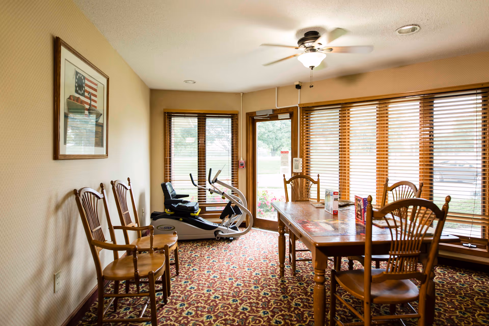 Interior dining area with a wooden table and chairs, large windows, and an exercise bike.