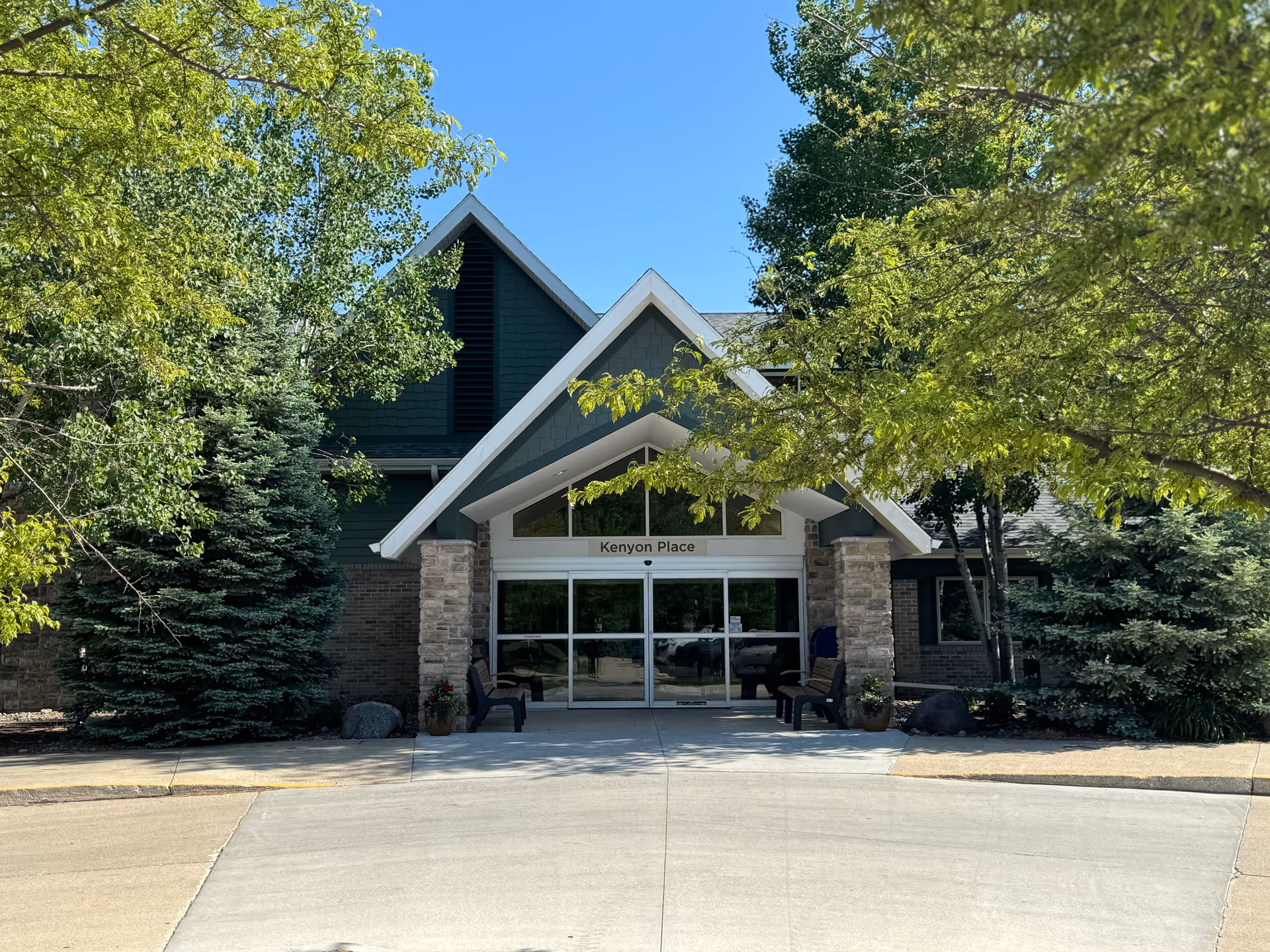 Front entrance of a residential building labeled "Kenyon Place" with trees and benches in front.