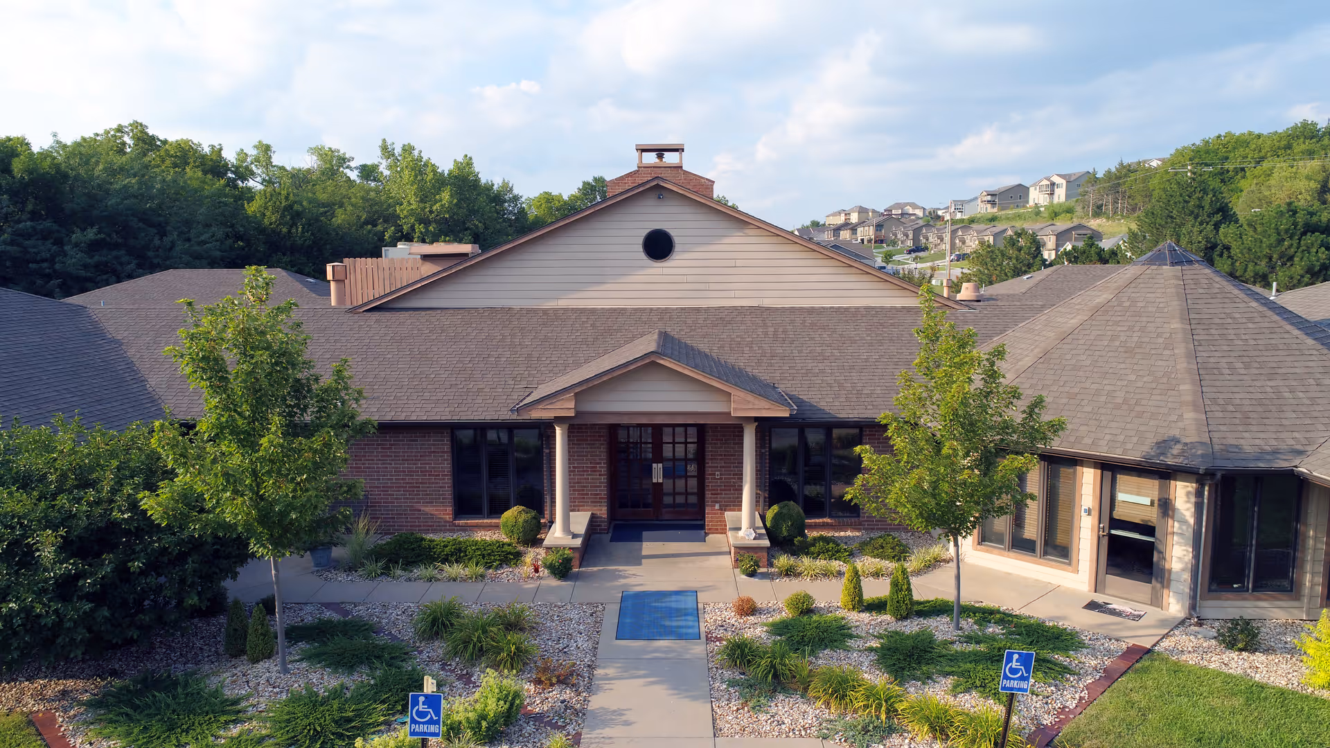 Front entrance of a single-story assisted living building with a covered porch, landscaped walkway, and handicap parking signs.