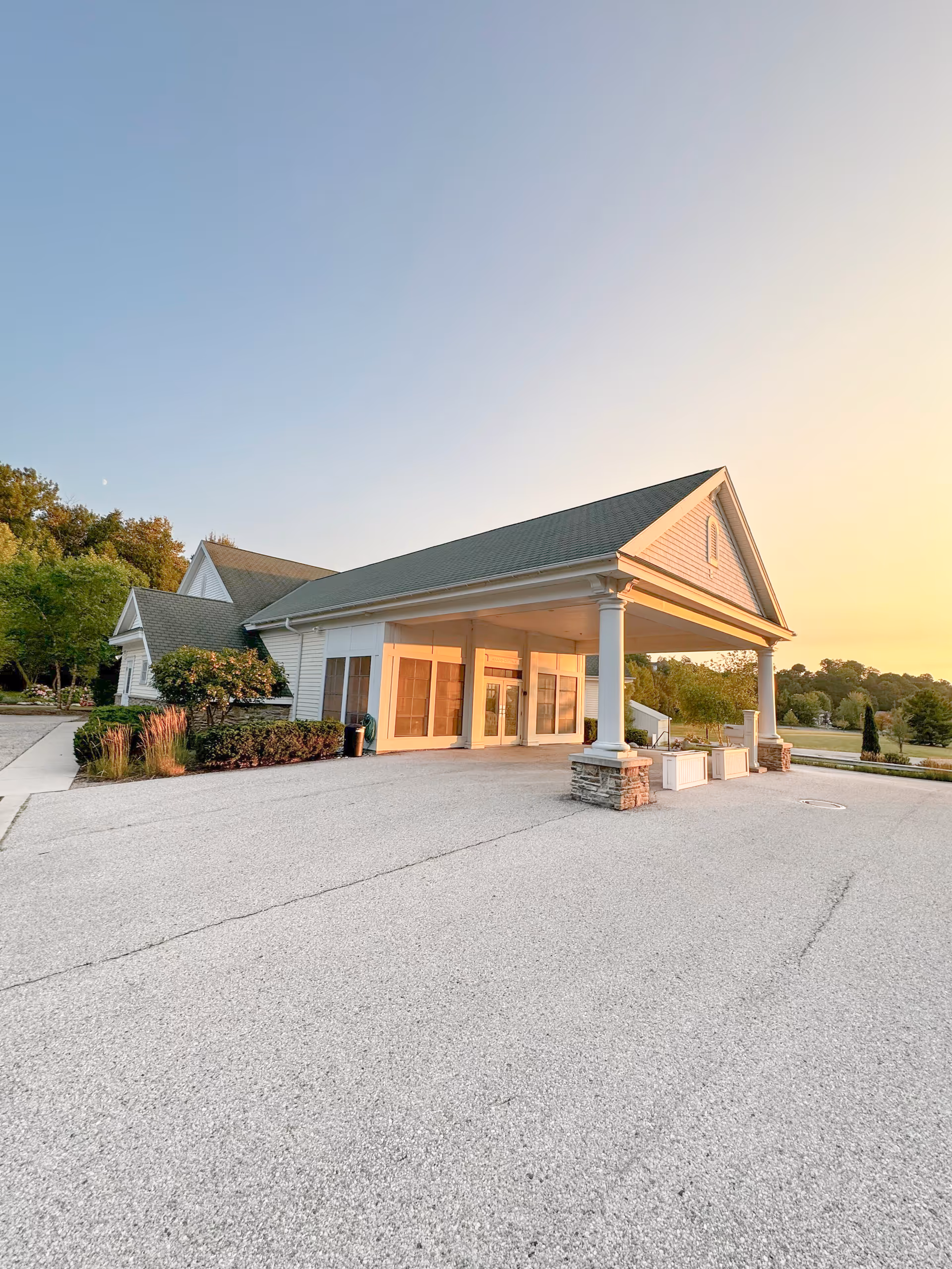 Sunset-lit exterior of Blissful Cottage senior living facility with covered entrance and wide driveway.