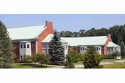 Long senior living facility with green-roofed buildings, brick chimneys, and manicured landscaping.