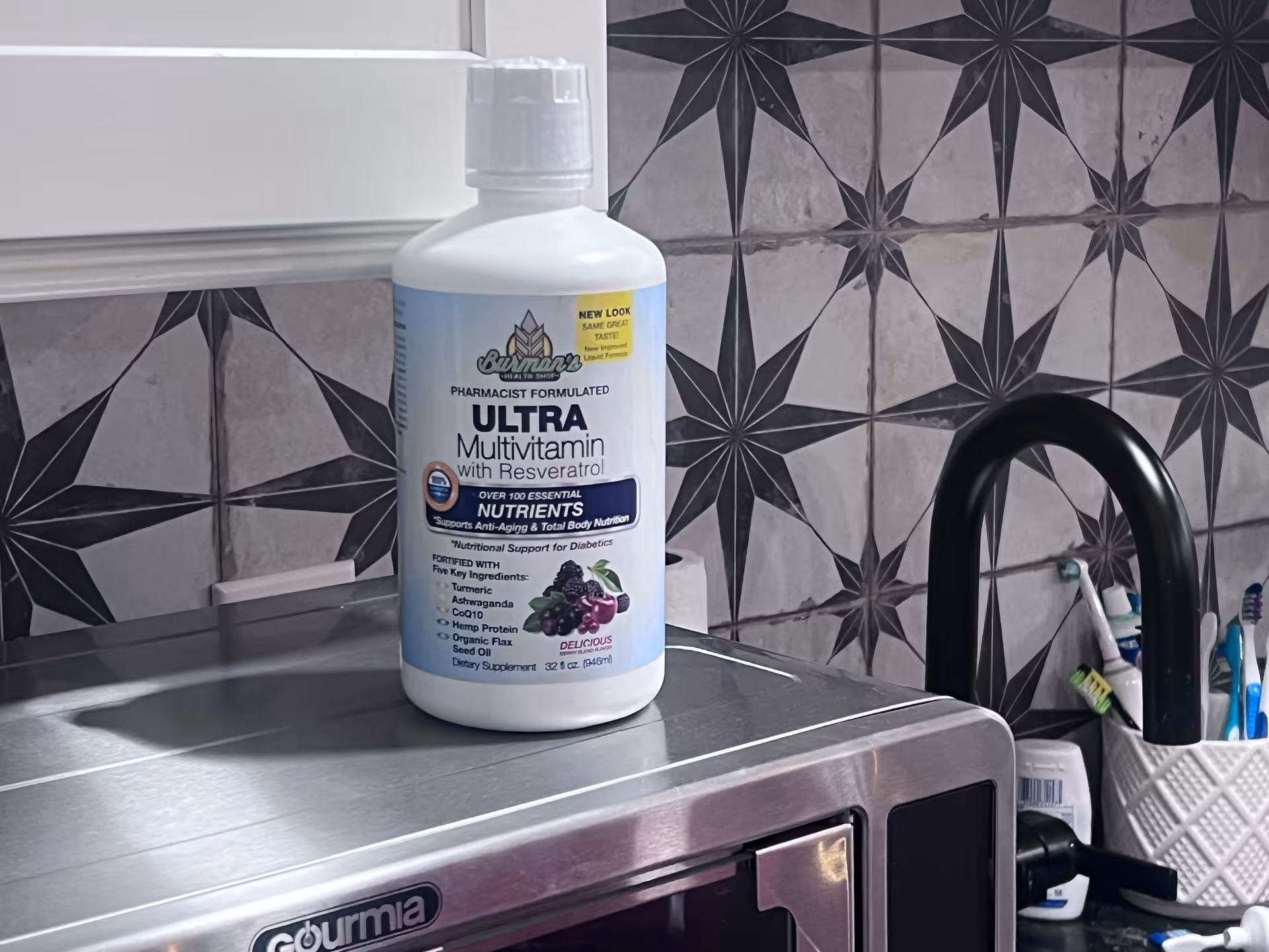 A white vitamin bottle sits on a stainless steel appliance amid tiled interior.