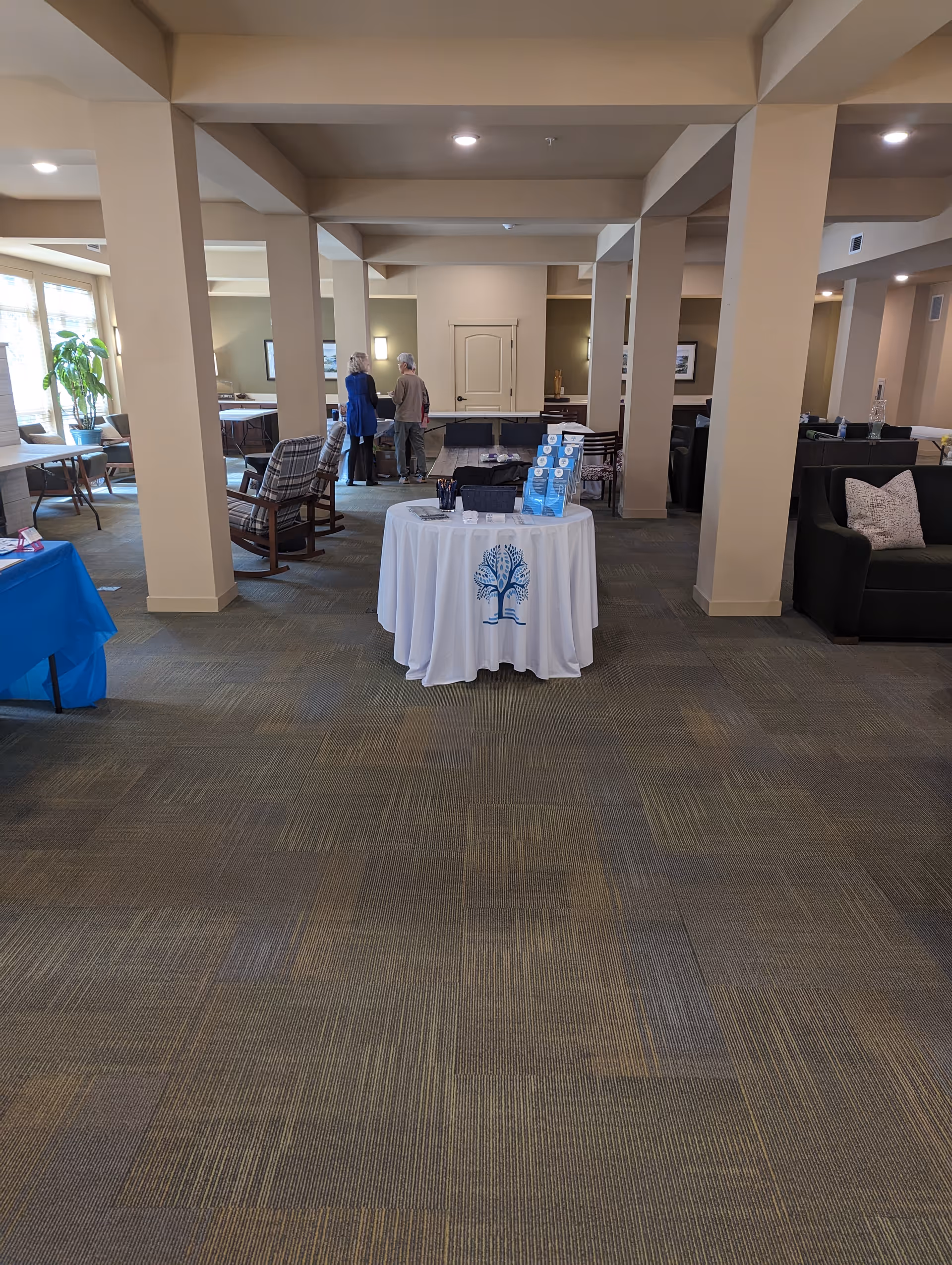 Interior senior living common area with a round table covered in white cloth and two people.