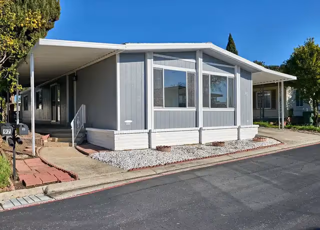 A single story senior living facility with gray siding, large windows, and a gravel front yard.