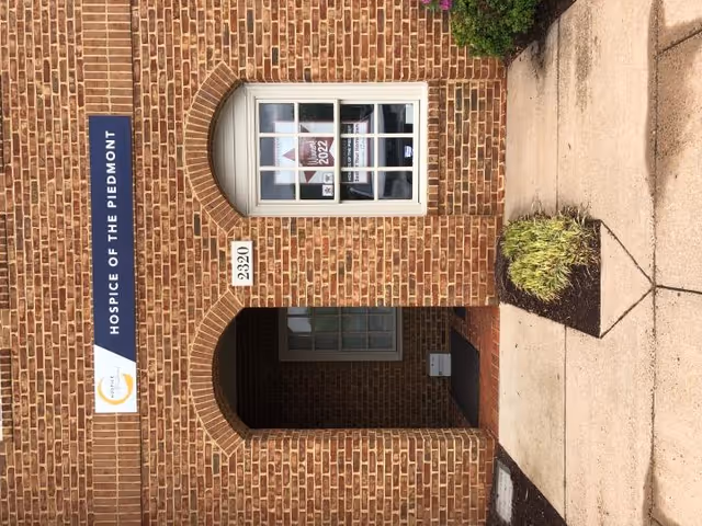 Brick building entrance with an arched doorway and Hospice of the Piedmont sign.