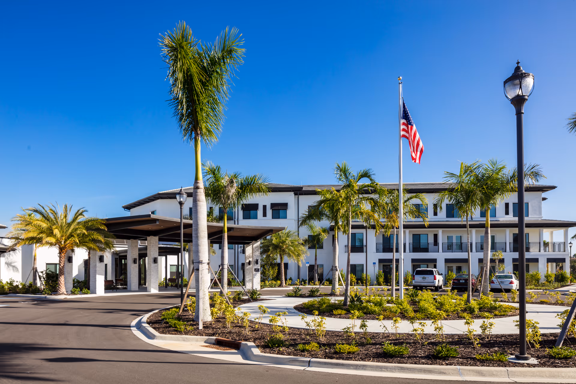 Exterior view of American House Naples, a modern senior living facility with palm trees and flag.