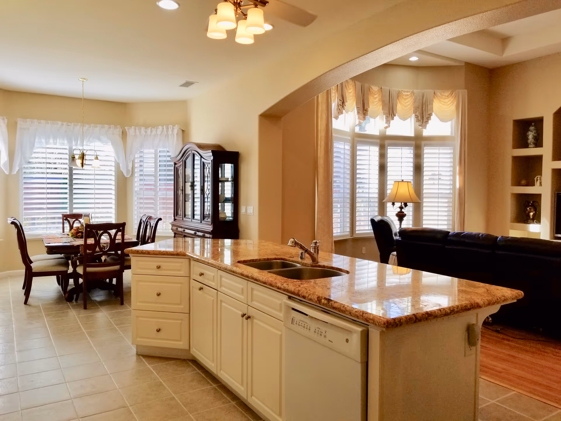 Open kitchen with island, sink, dishwasher, and adjacent dining area in a sunny space.