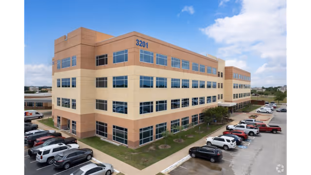 Exterior view of a multi-story brick facility with many windows and a parking lot.