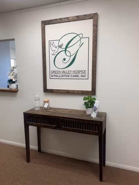 Framed Green Valley Hospice sign above a dark wooden console table in a hallway