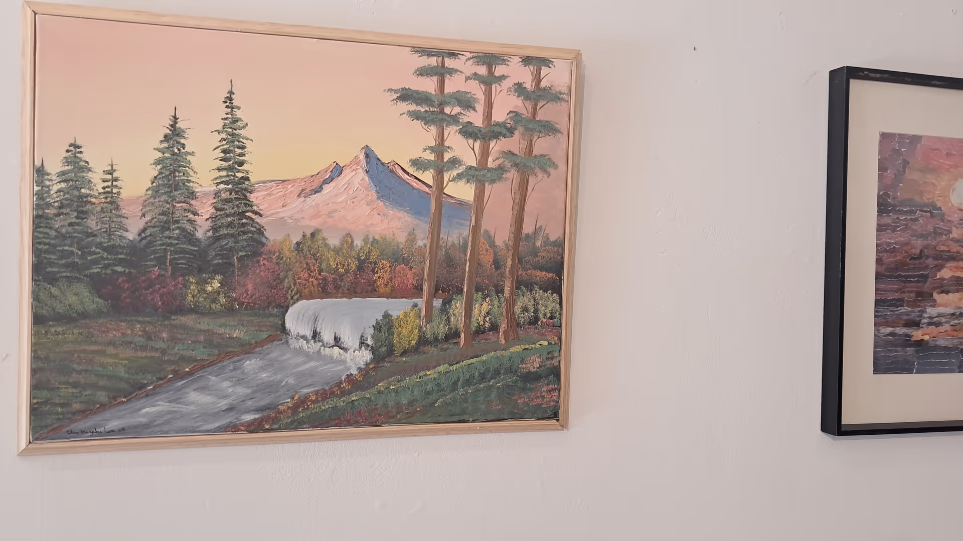 Two framed landscape paintings hang on a light wall inside a facility.
