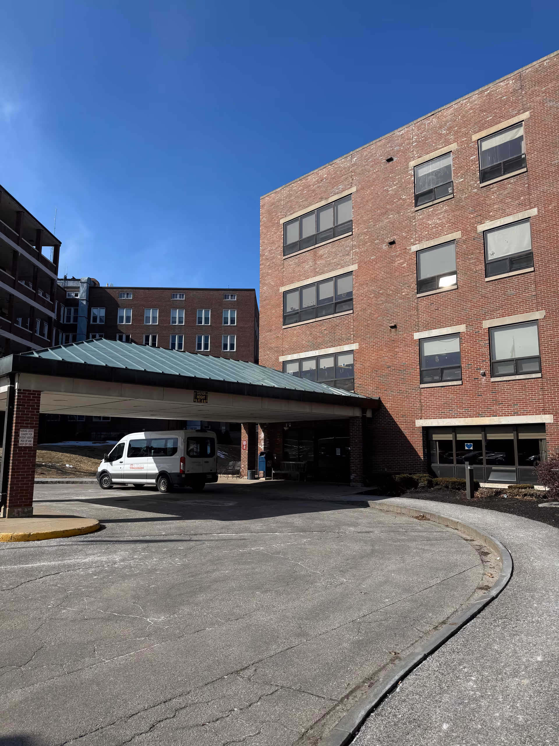 Exterior of a brick senior living facility with a covered entrance and a white van.