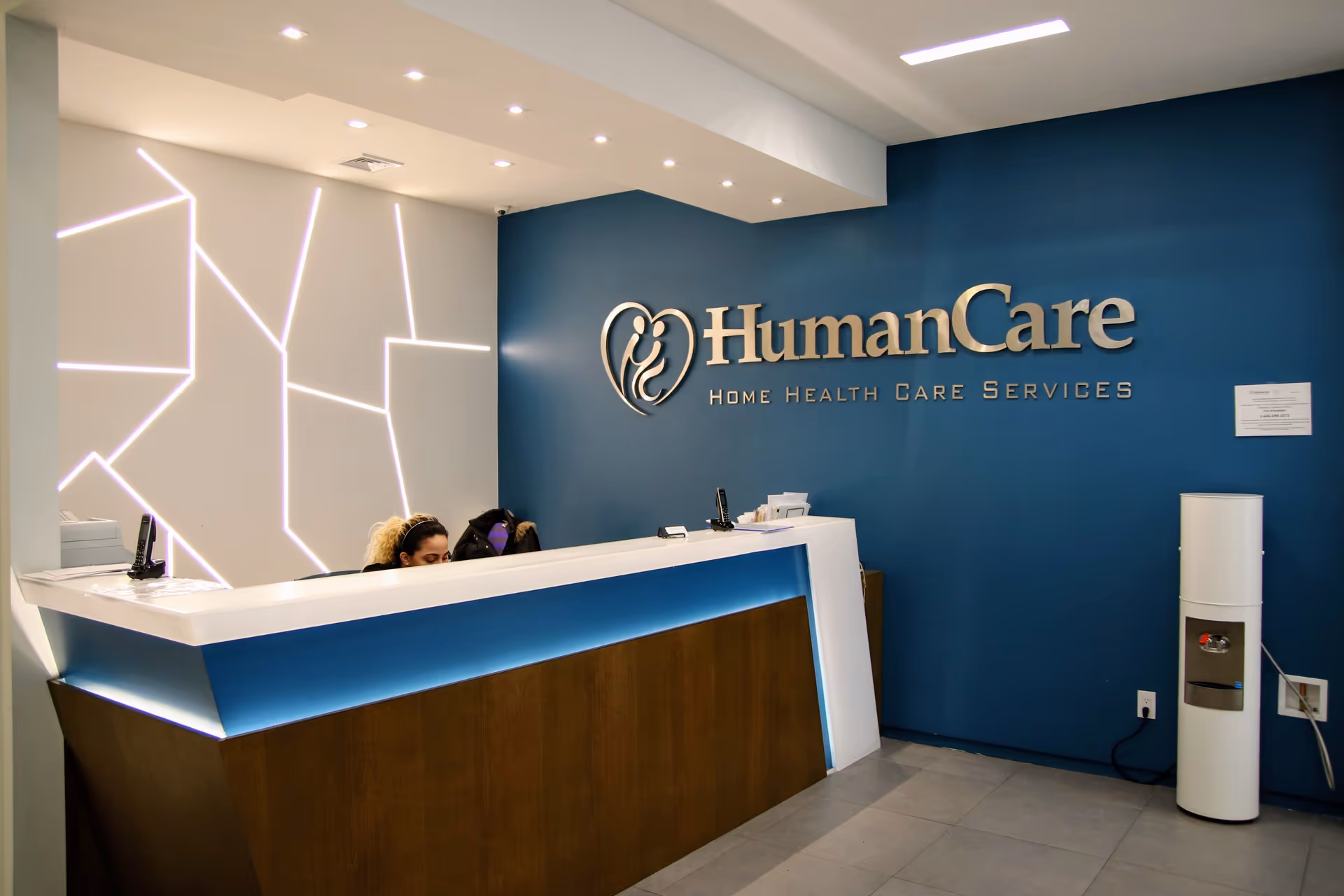 Reception area with a blue wall, the HumanCare logo, and staff behind the desk.