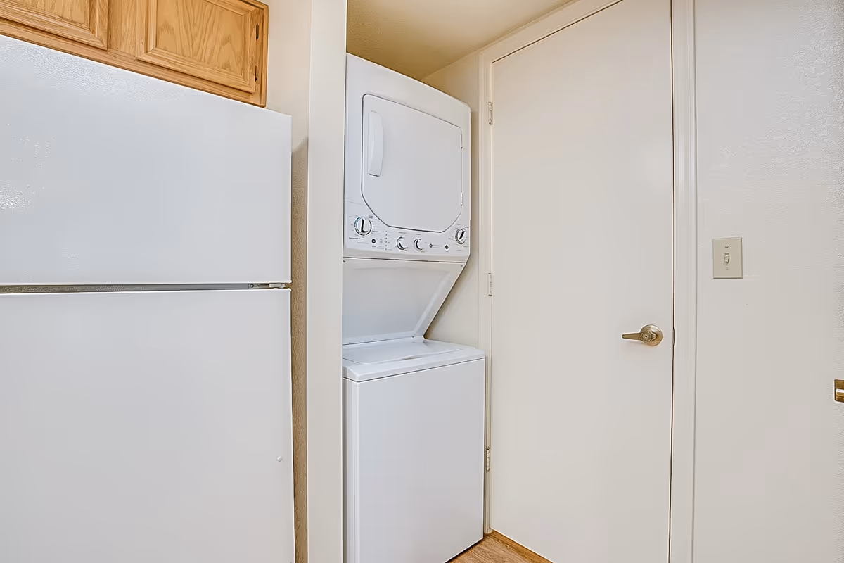 Stacked washer and dryer beside a white refrigerator in a compact utility alcove.