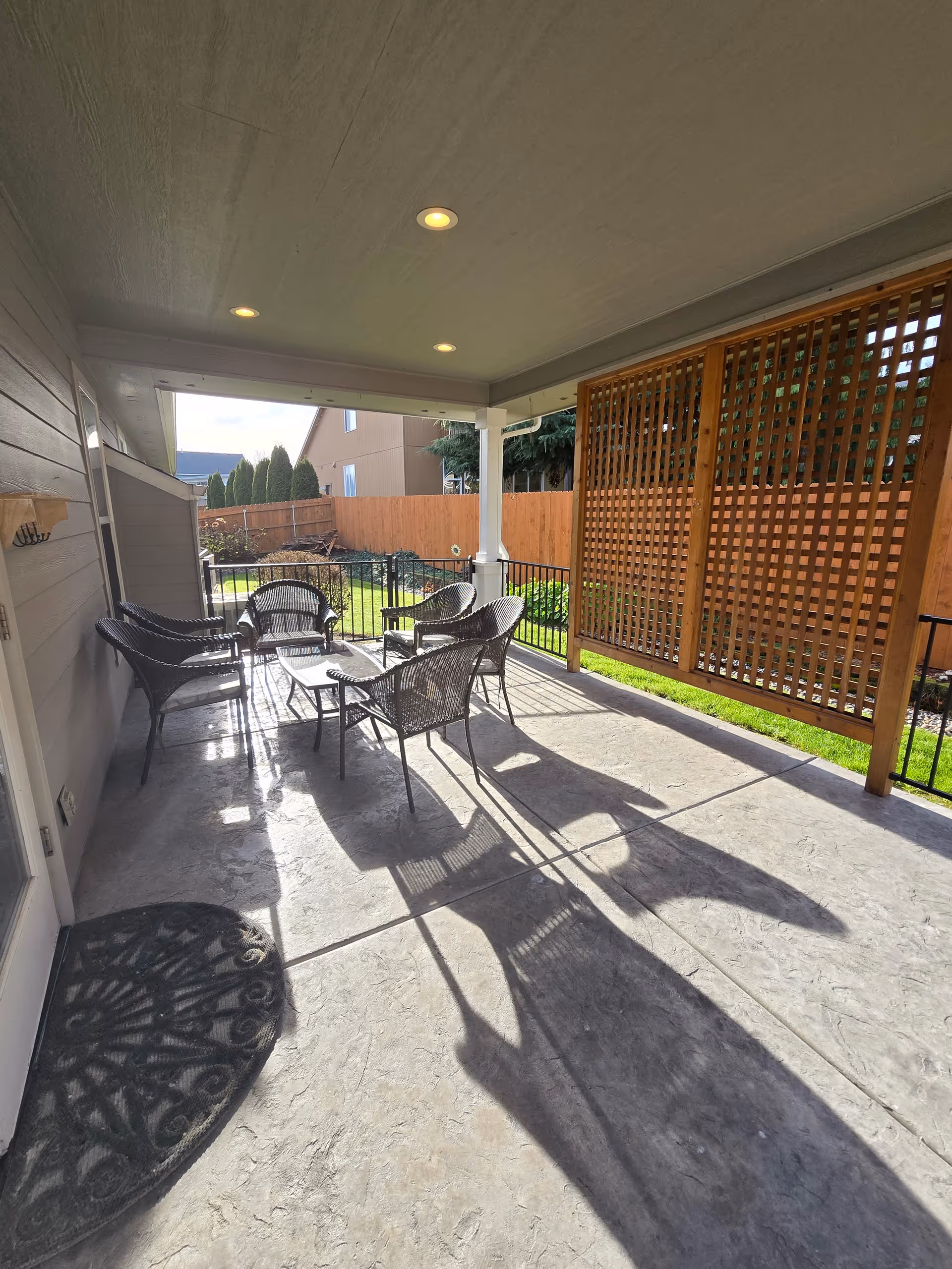 Covered outdoor patio with wicker chairs, table, and lattice privacy screen.