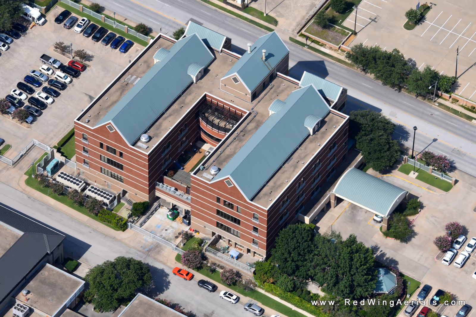 Aerial view of a brick senior living facility with teal roofs and parking