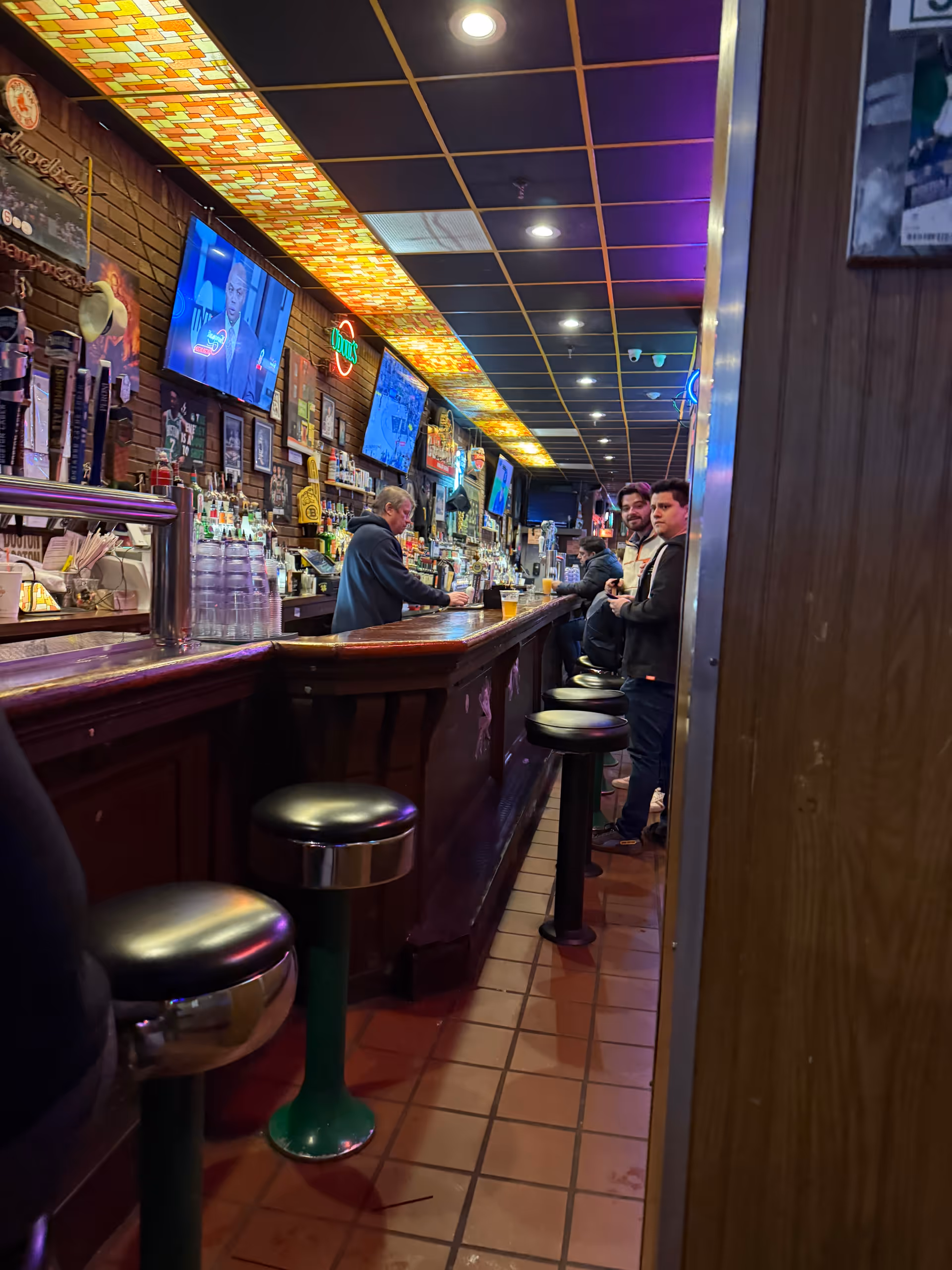 Indoor bar area with stools along a long counter and patrons at the bar.