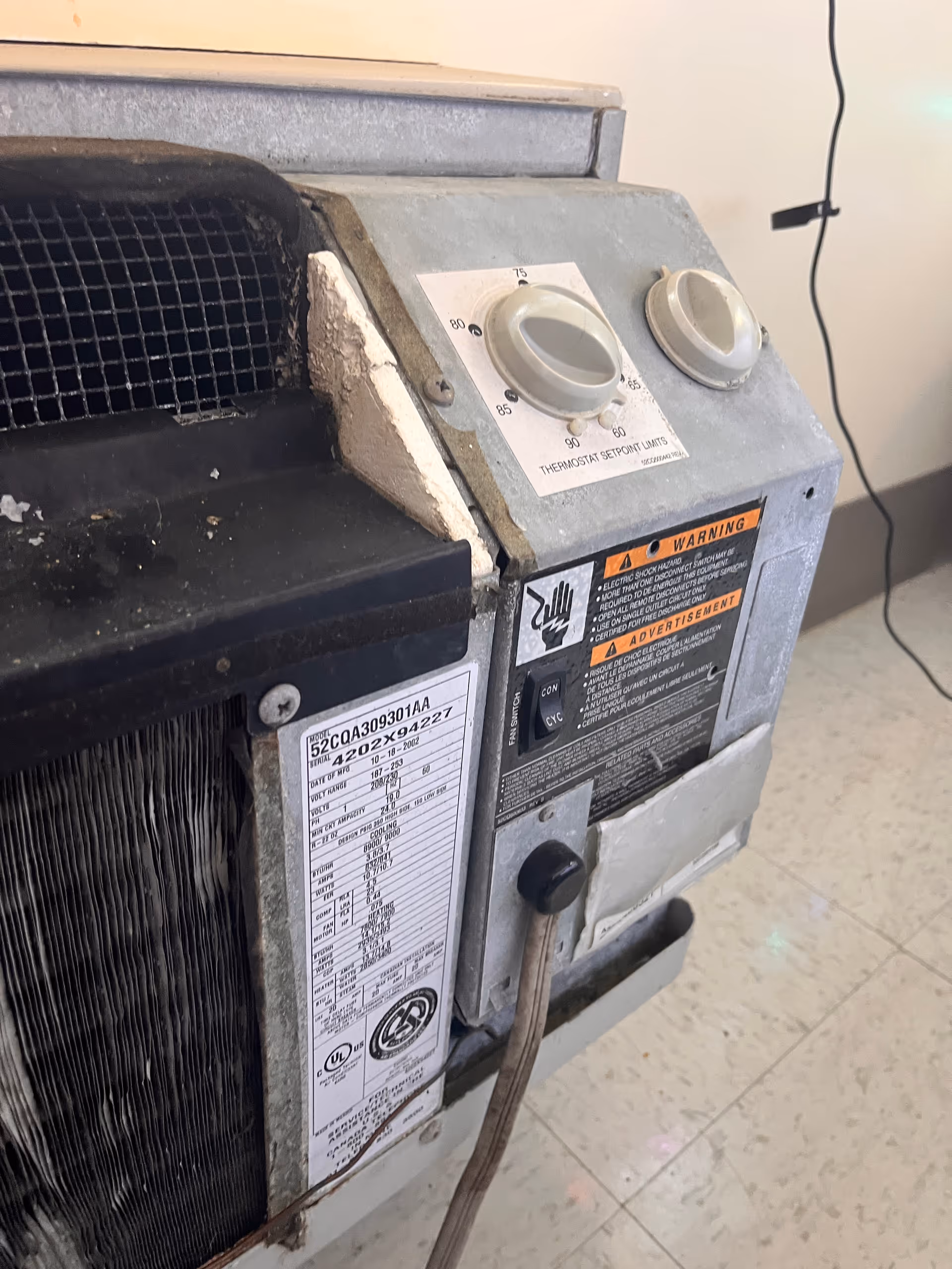 Close-up of a dusty aging HVAC control panel with dials and warning labels.