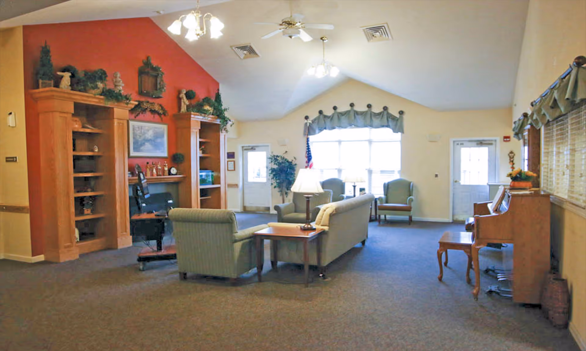 Lounge area with sofas, chairs, piano, bookcases, and a red-accent wall.