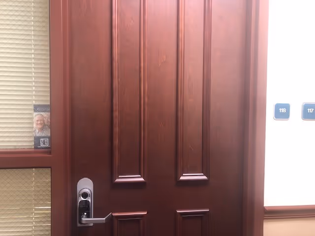 A wooden interior door in a hallway with room numbers on the wall.