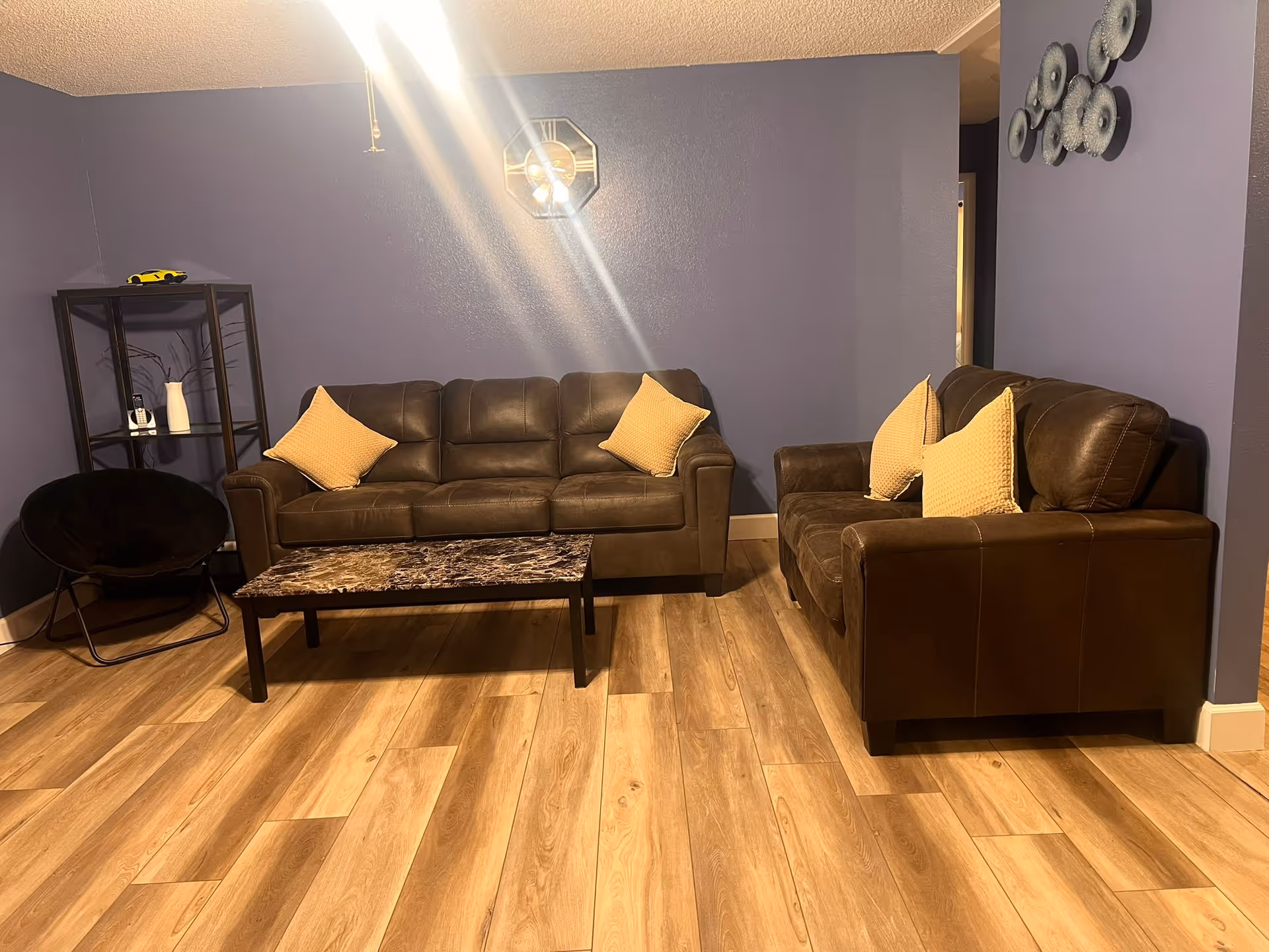Blue-walled living room with two brown sofas, cushions, a coffee table, and chair.