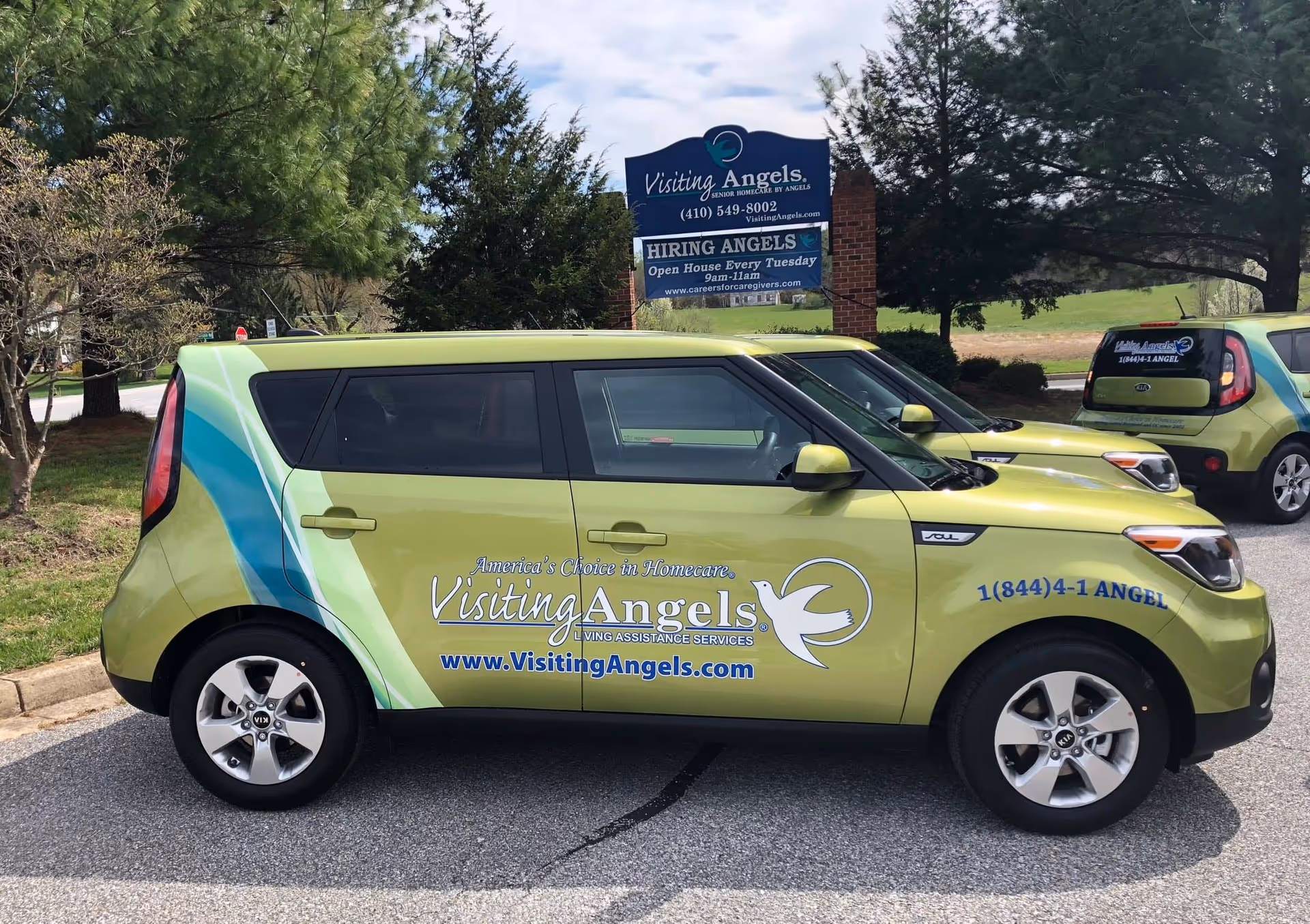 Colorful Visiting Angels vans parked near an exterior facility sign for Visiting Angels Frederick.