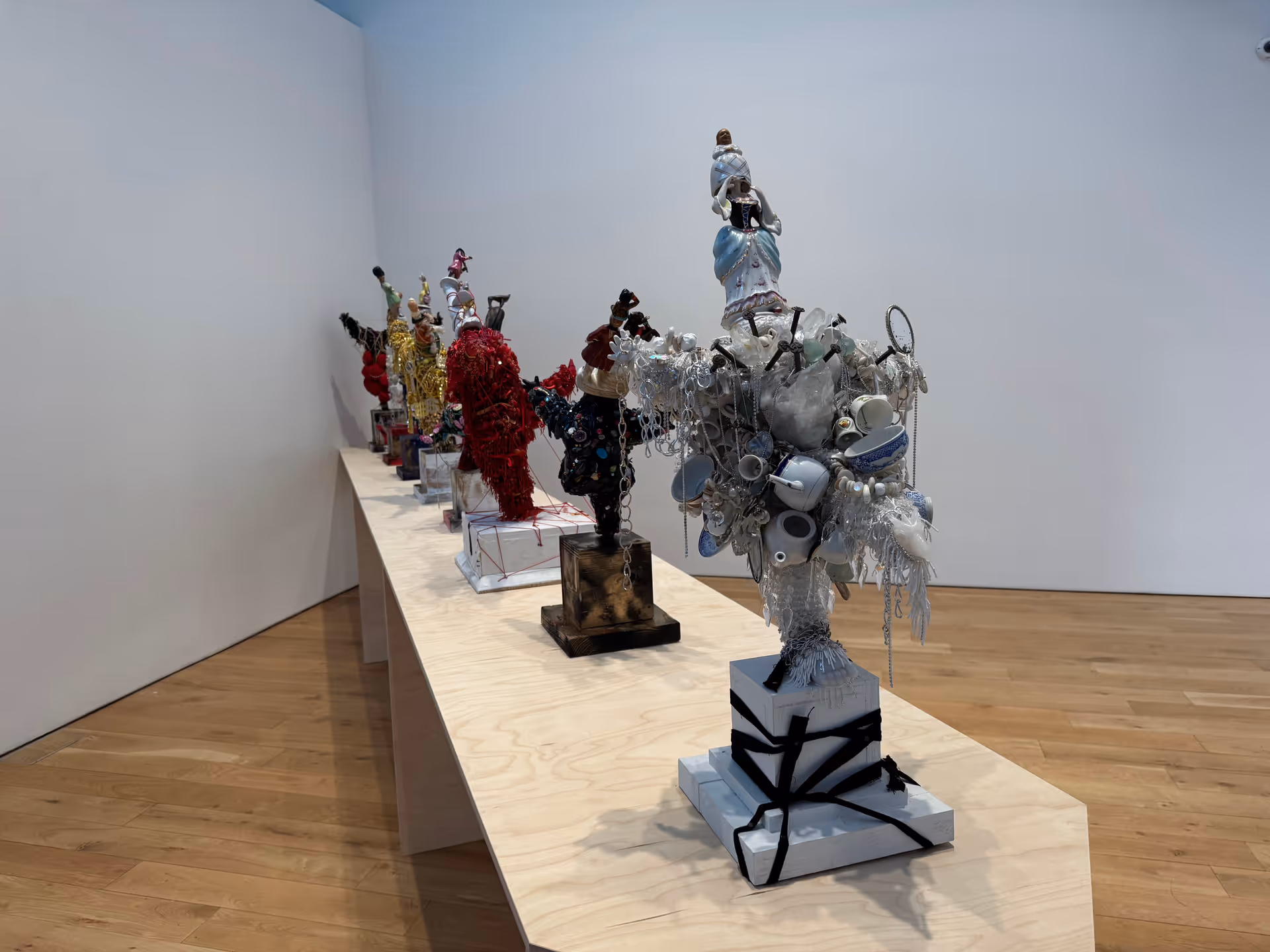 Interior gallery with a long table displaying multi-colored sculptures made from recycled objects.