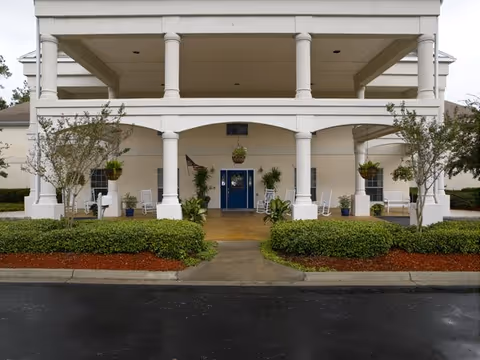 White front-entry porch with tall columns, blue doors, and potted plants.