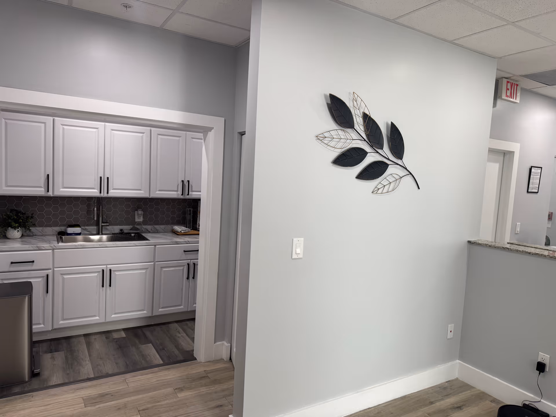 Bright white kitchen with cabinets, sink, gray backsplash, and decorative wall art in a hallway.