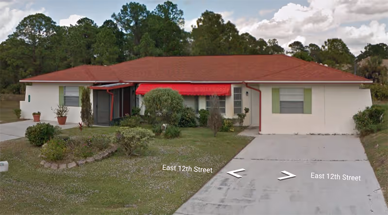 Front exterior of a single-story Brewer Group Home, beige walls, red roof, green shutters, driveway.