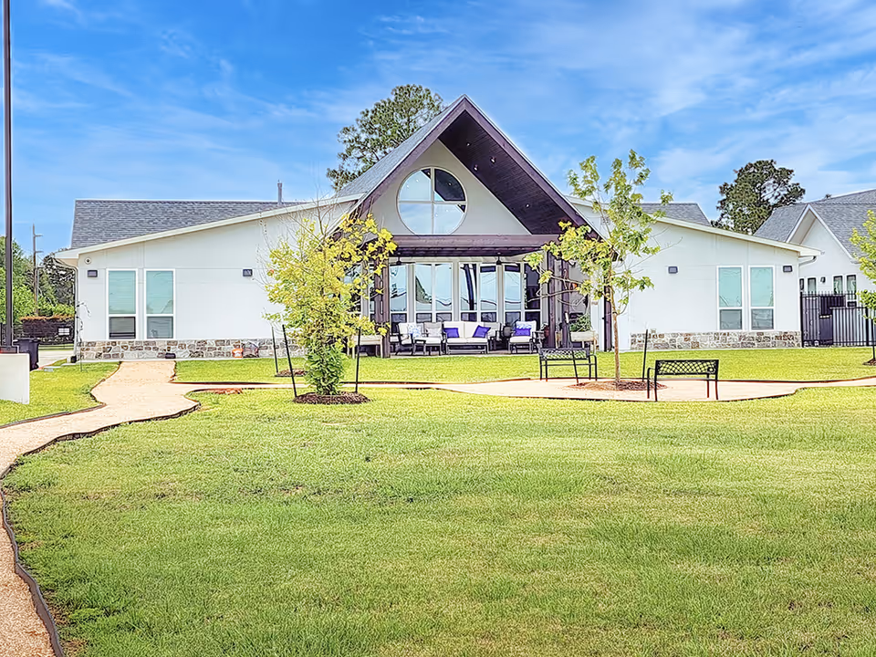 Front view of a white assisted living facility with a peaked roof and green lawn.
