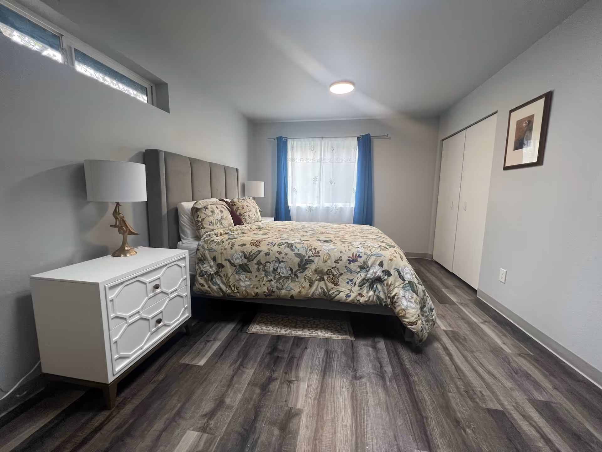 A neutral bedroom with a queen bed, two nightstands, lamps, window, and closet.
