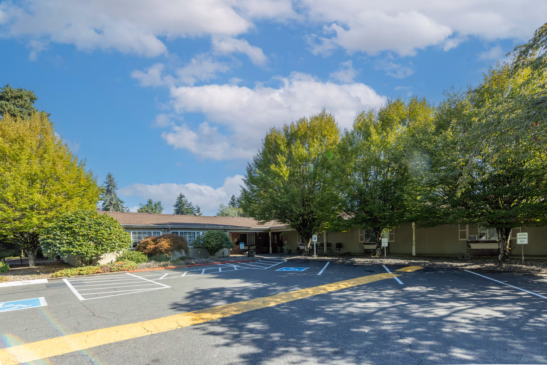 Front view of a one-story senior living center with a parking lot and trees.