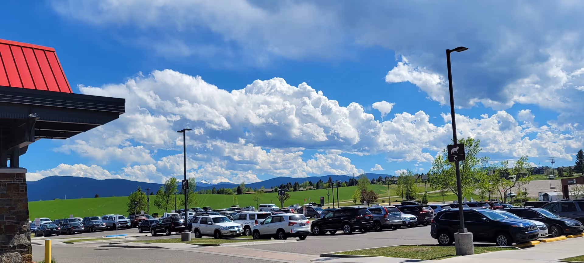 Exterior view of a building with a large parking lot, green field, and blue sky.