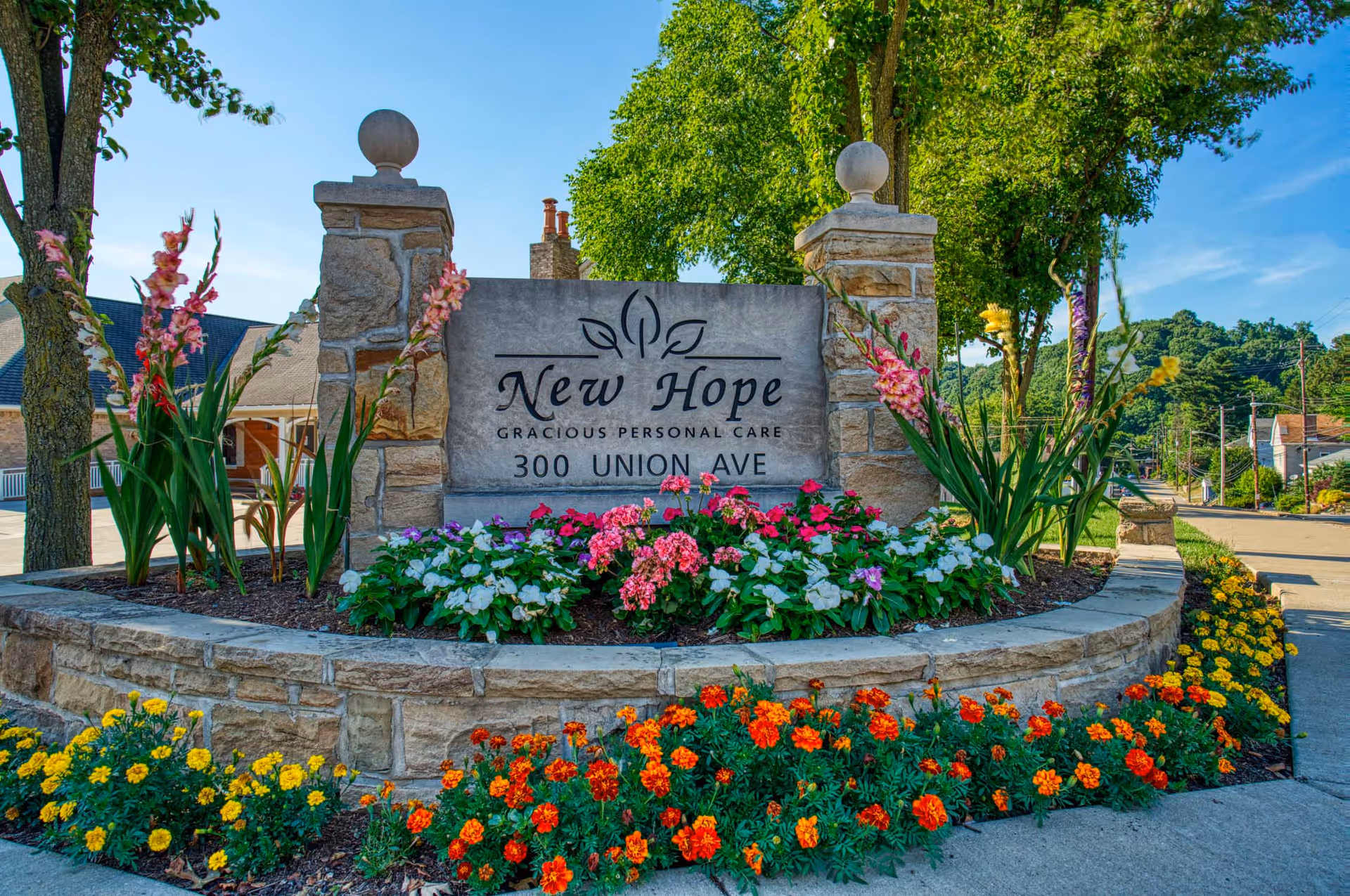 Stone entrance sign for New Hope Gracious Personal Care at 300 Union Ave surrounded by colorful flower beds and trees.