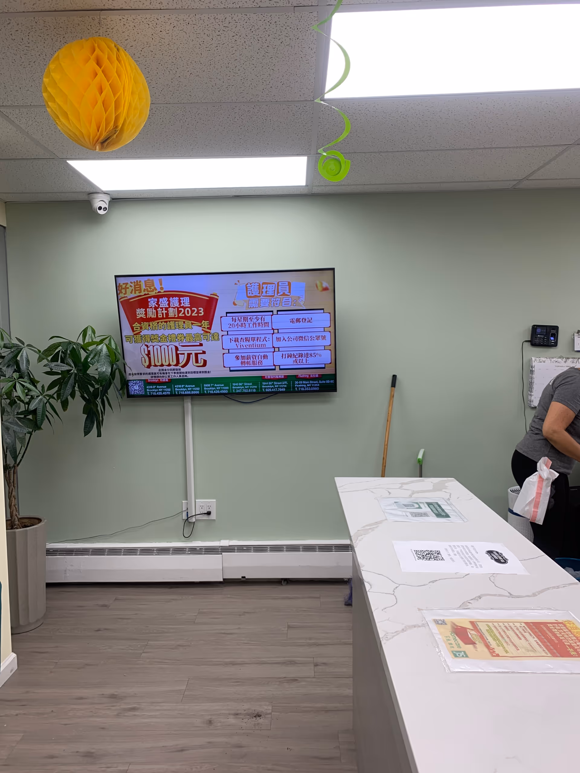 Reception area inside a senior care facility with a mounted TV, plant, and marble counter.