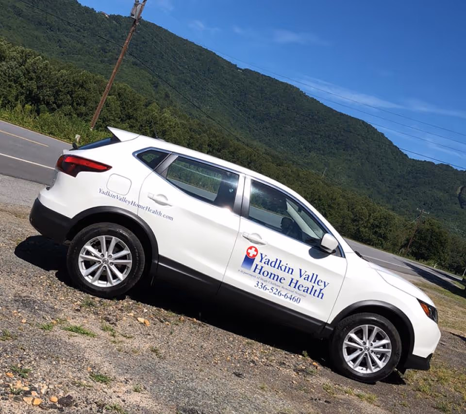 White Yadkin Valley Home Health vehicle parked on a rocky roadside with mountains behind.