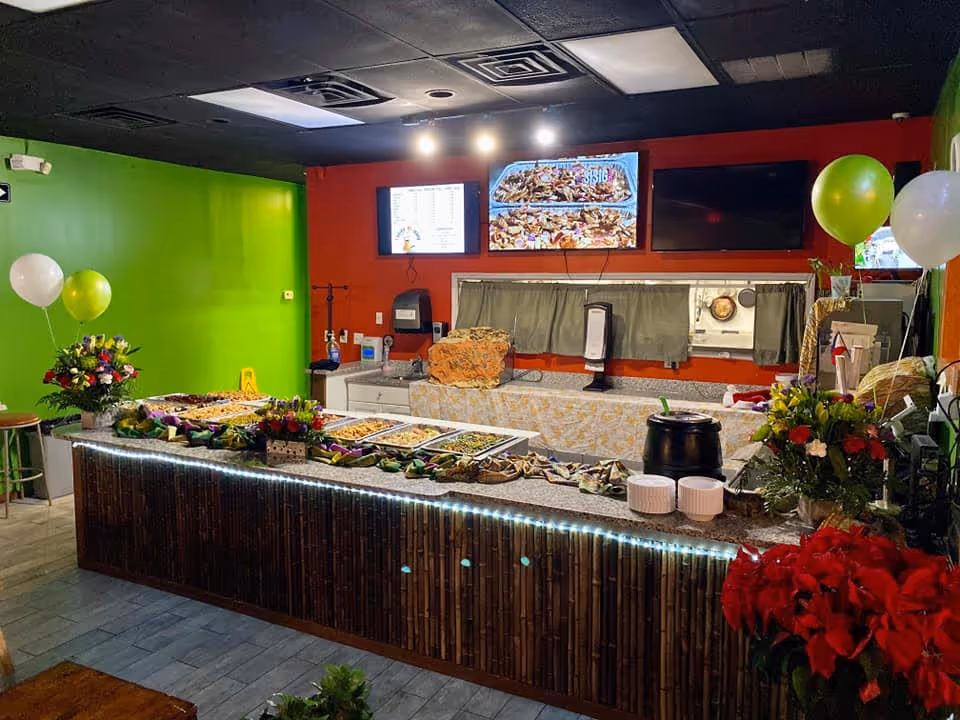 Buffet-style dining counter with food trays, festive balloons, and a kitchen behind.