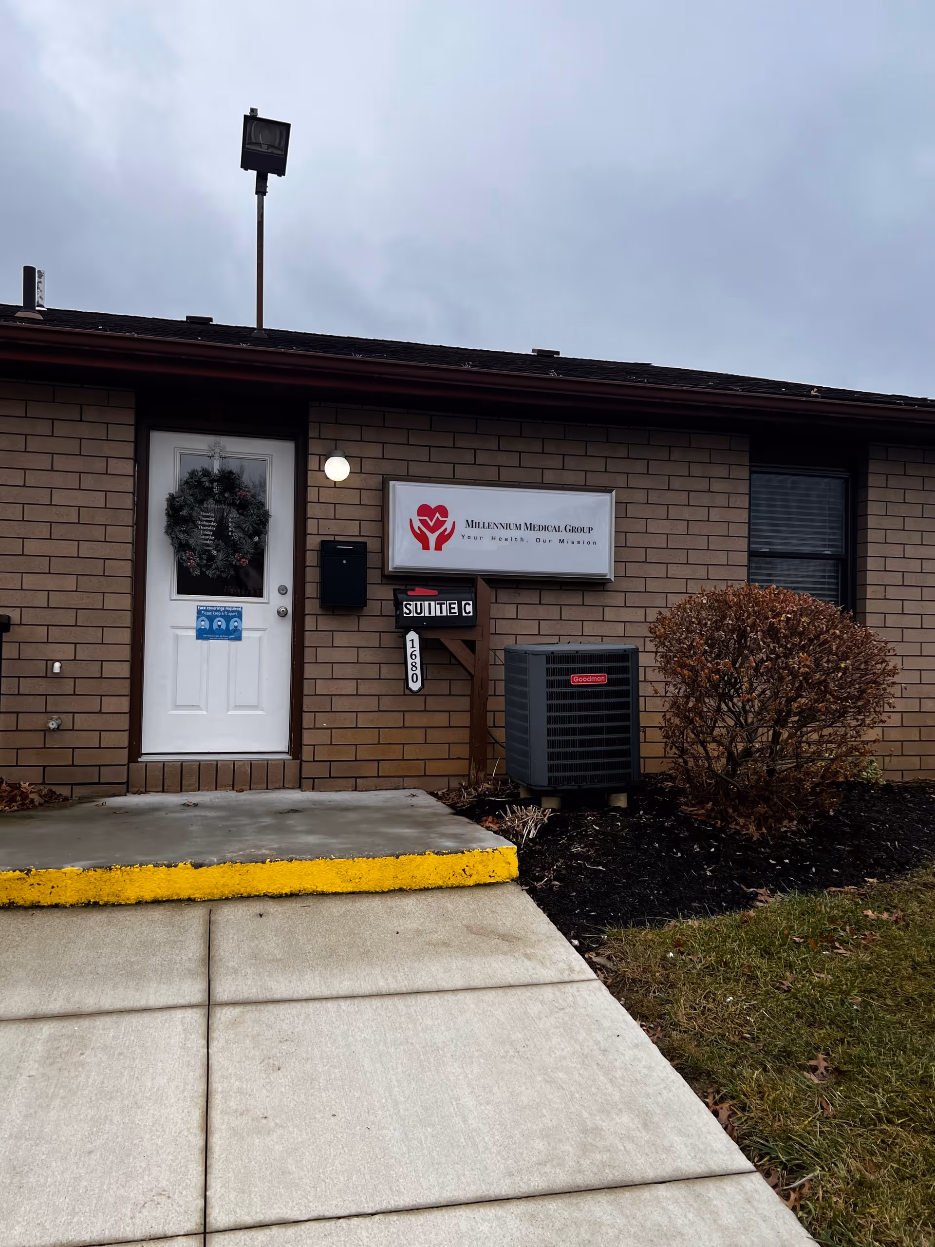 Brick exterior of Millennium Medical Group facility with door, wreath, sign, and air conditioning unit.