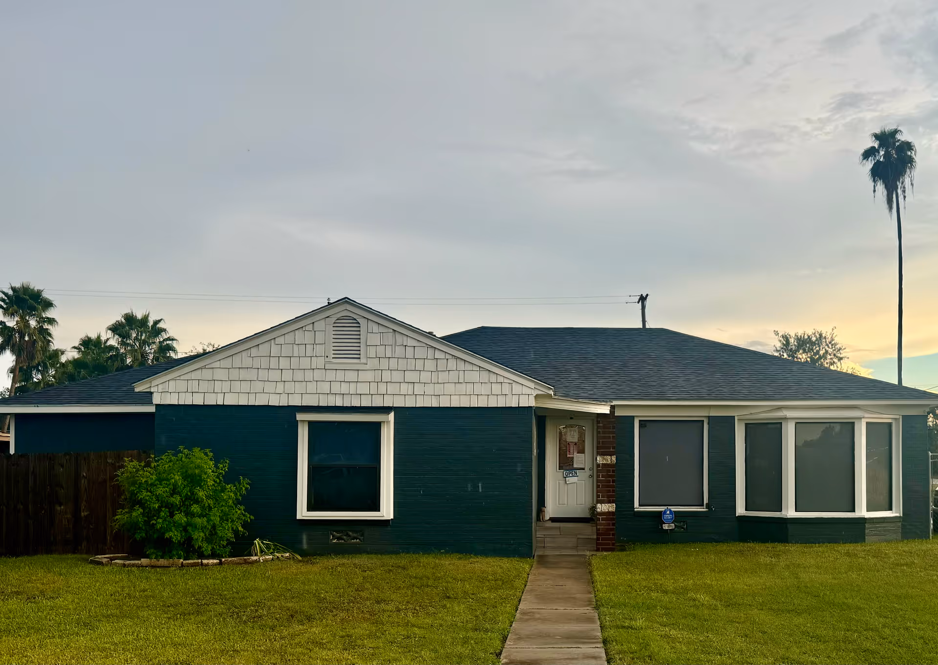 Front view of a single-story dark teal house with a walkway and lawn.