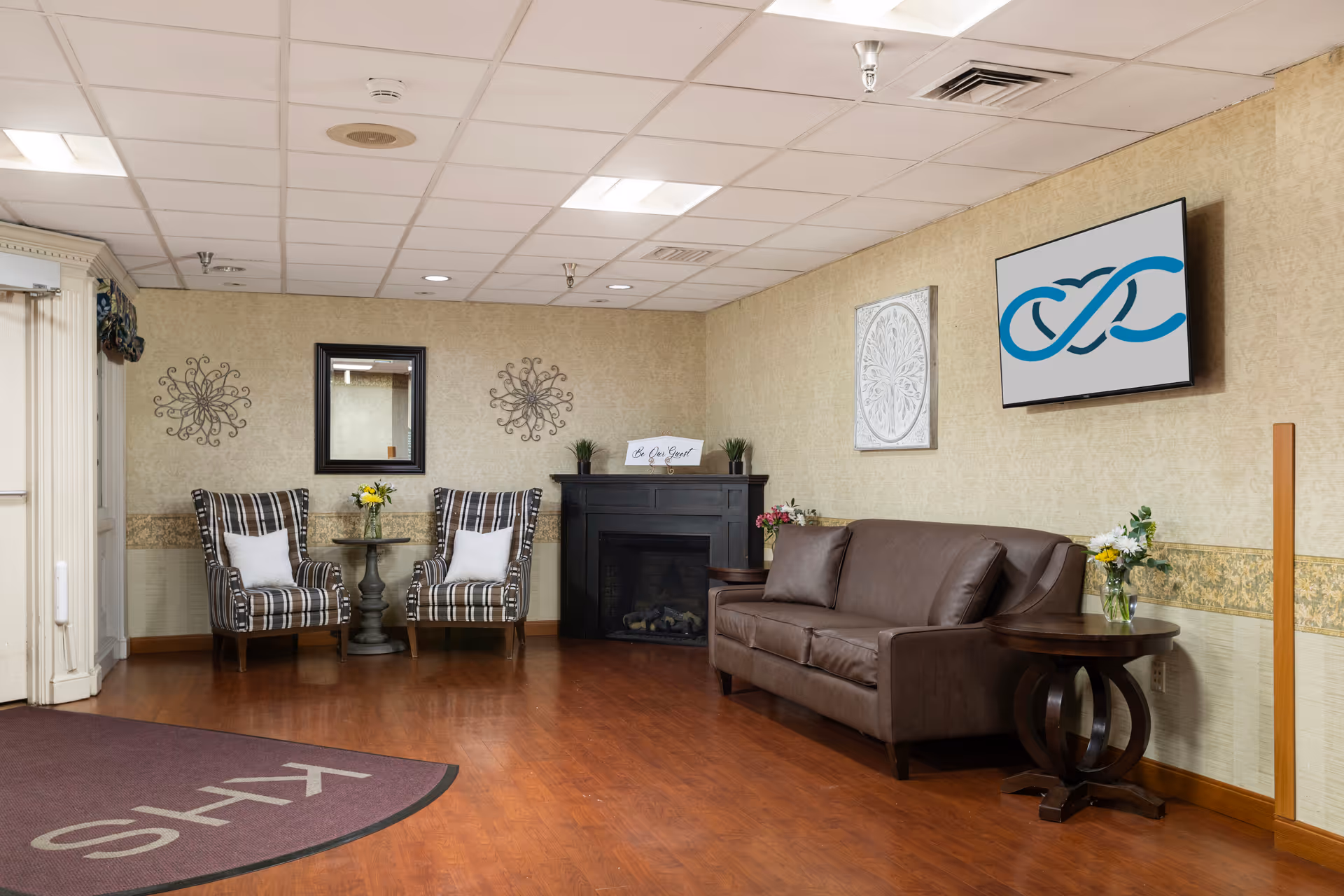Lounge area in a senior living facility with sofa, striped chairs, fireplace, and wall art.