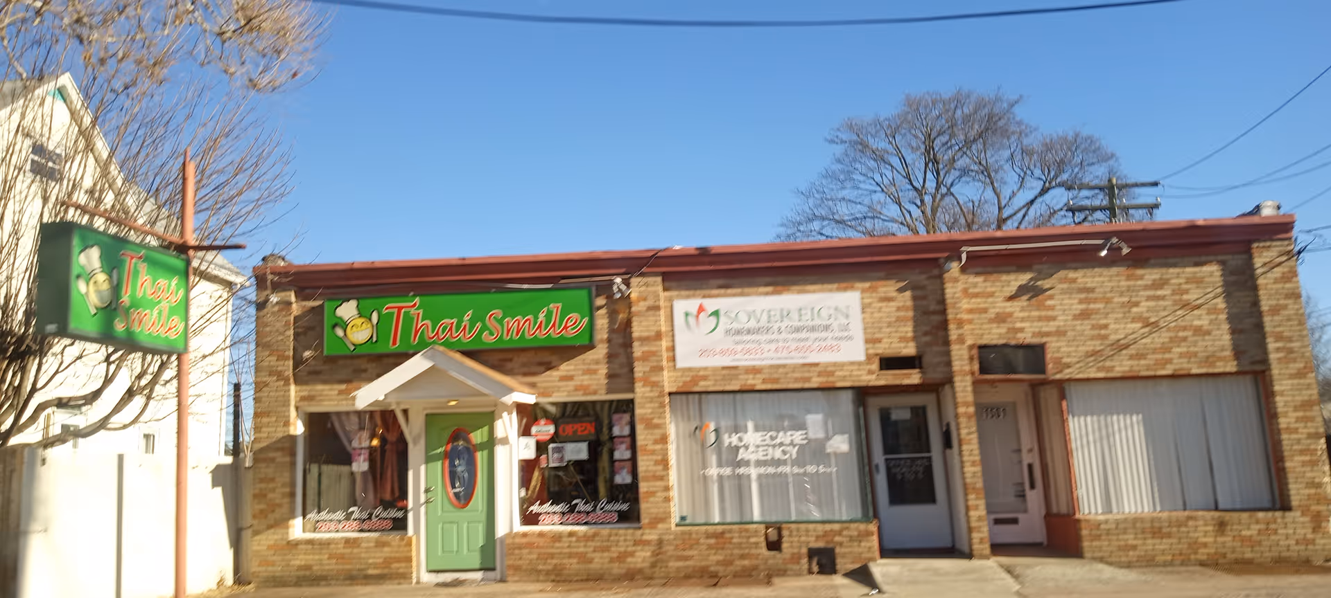 Row of storefronts on a sunny street, prominently featuring Thai Smile and Sovereign Homemakers signs.