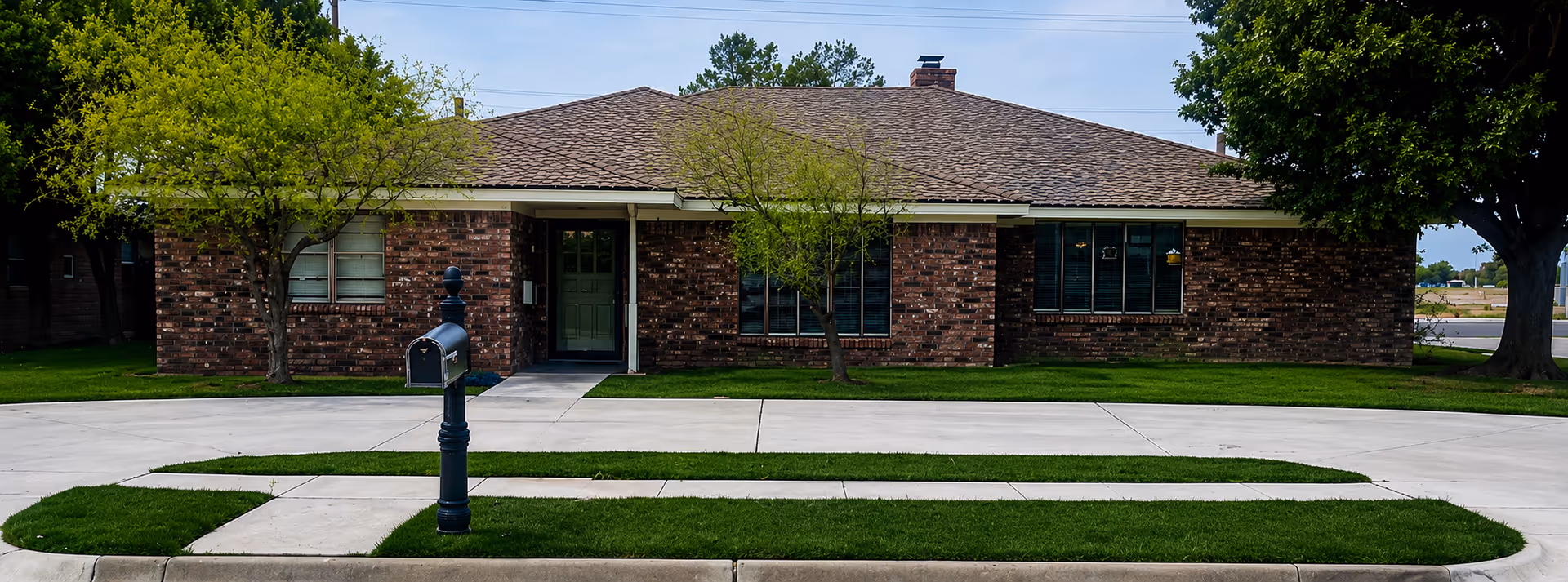 Brick senior living facility exterior with manicured lawn, trees, and a mailbox.