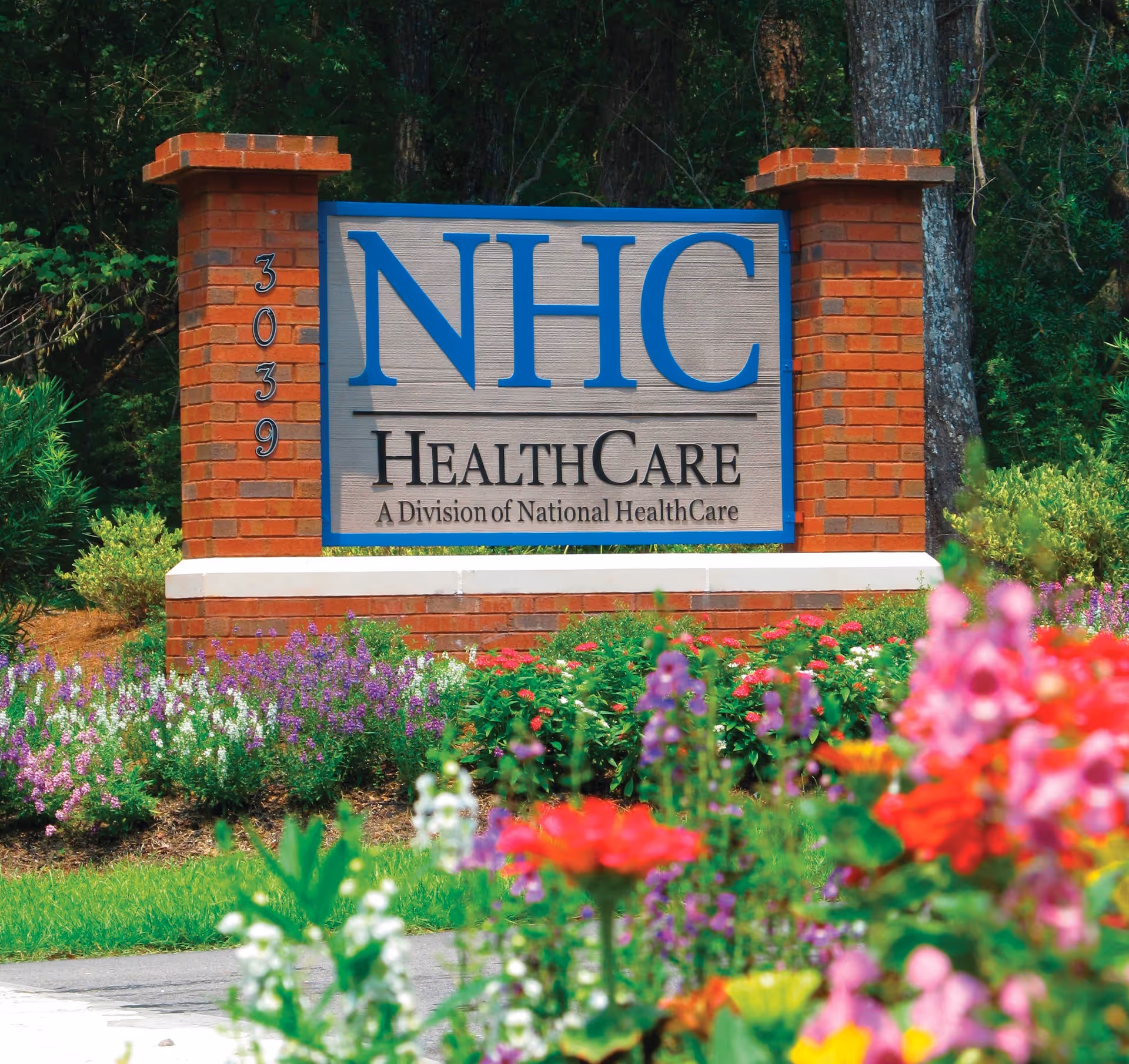 Brick NHC HealthCare sign at the front with colorful flowers and greenery.