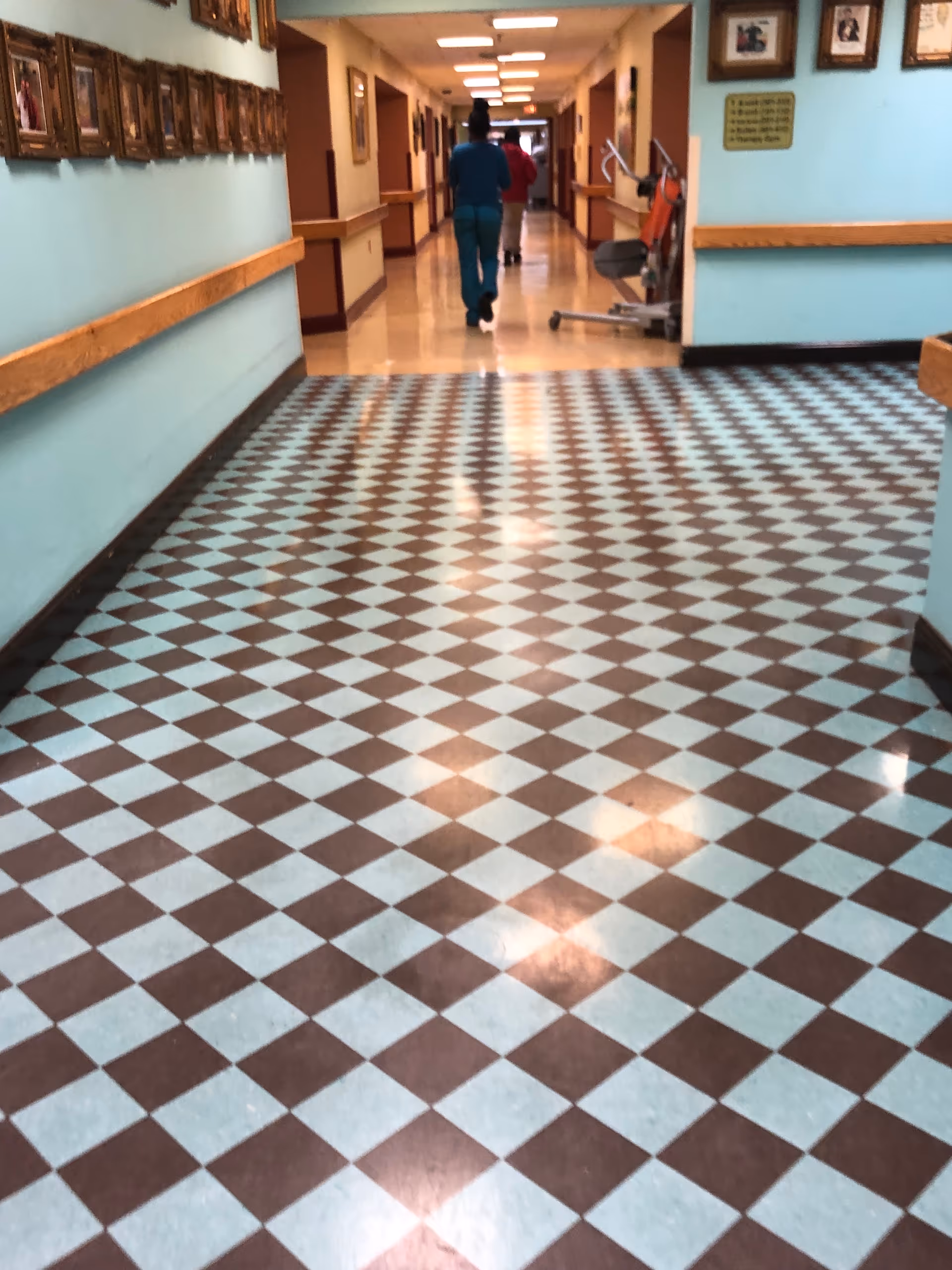 Long hallway with teal walls, brown and blue checkered floor tiles, and two people walking.
