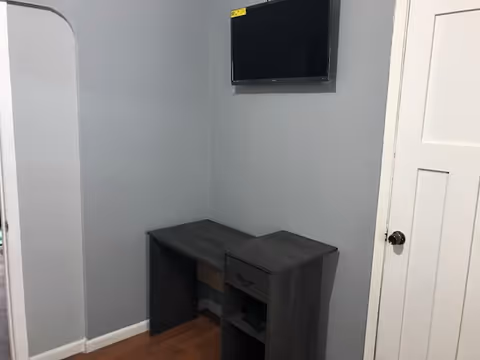 Small dark desk with a cabinet under a wall-mounted TV in a gray-walled corner.