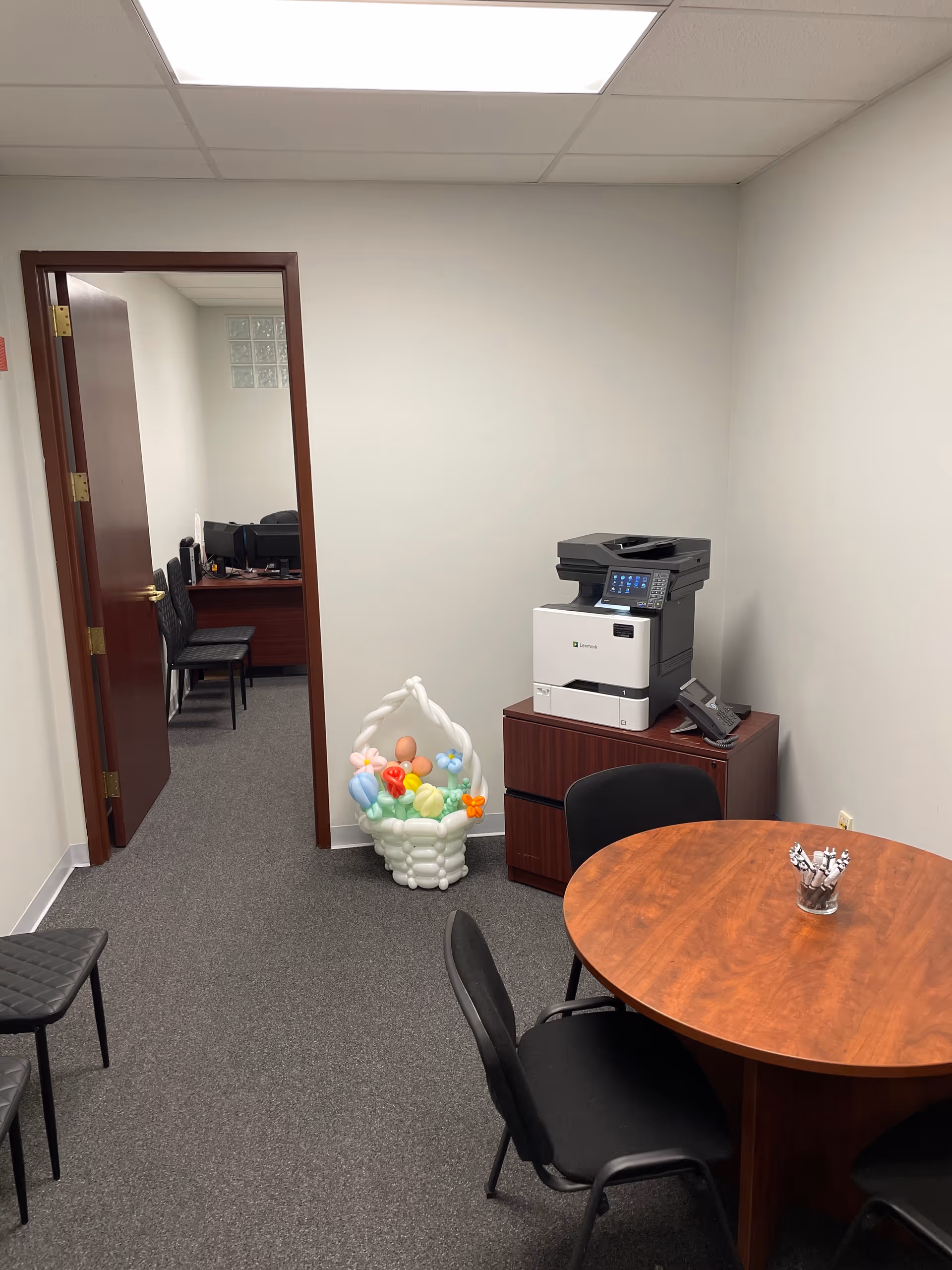 Interior office space with a round table, chairs, copier, and doorway to another room.