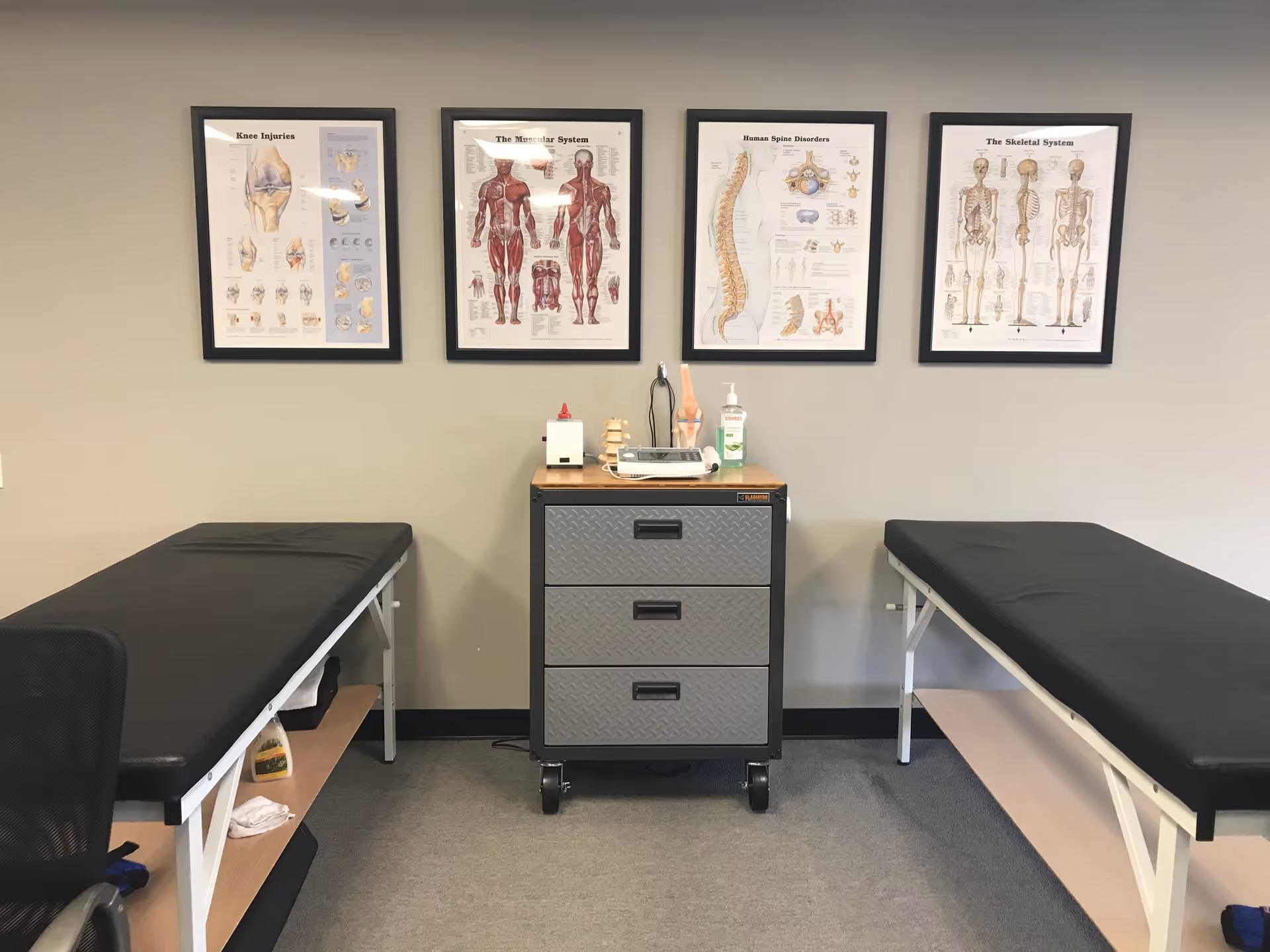 Two treatment tables flank a central cart with medical posters on the wall.