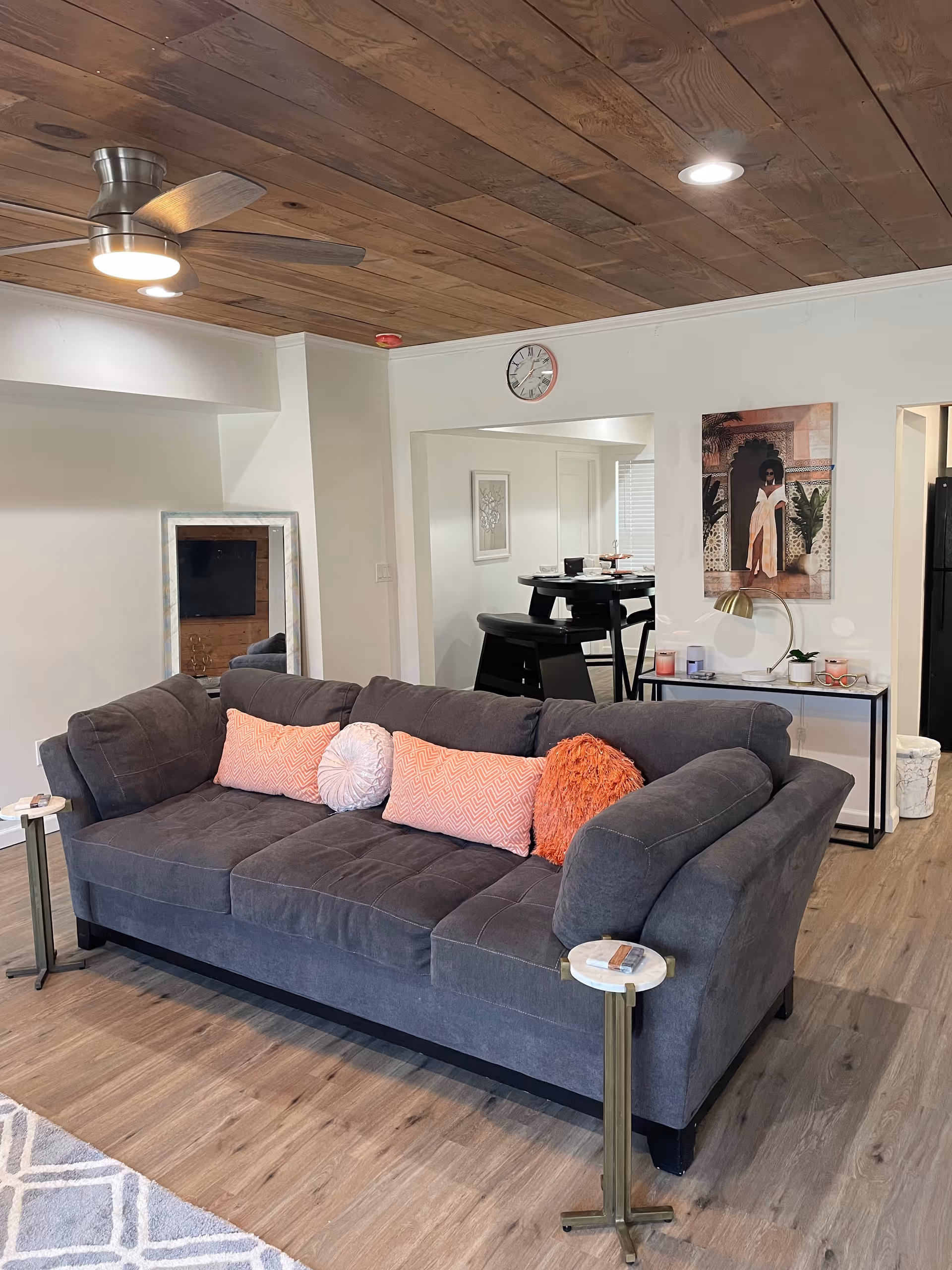 Cozy living room with gray sectional sofa, pink cushions, wooden ceiling, and dining area in back.