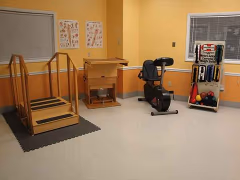 Therapy room in a senior living facility with a recumbent bike, ramp, and exercise equipment.