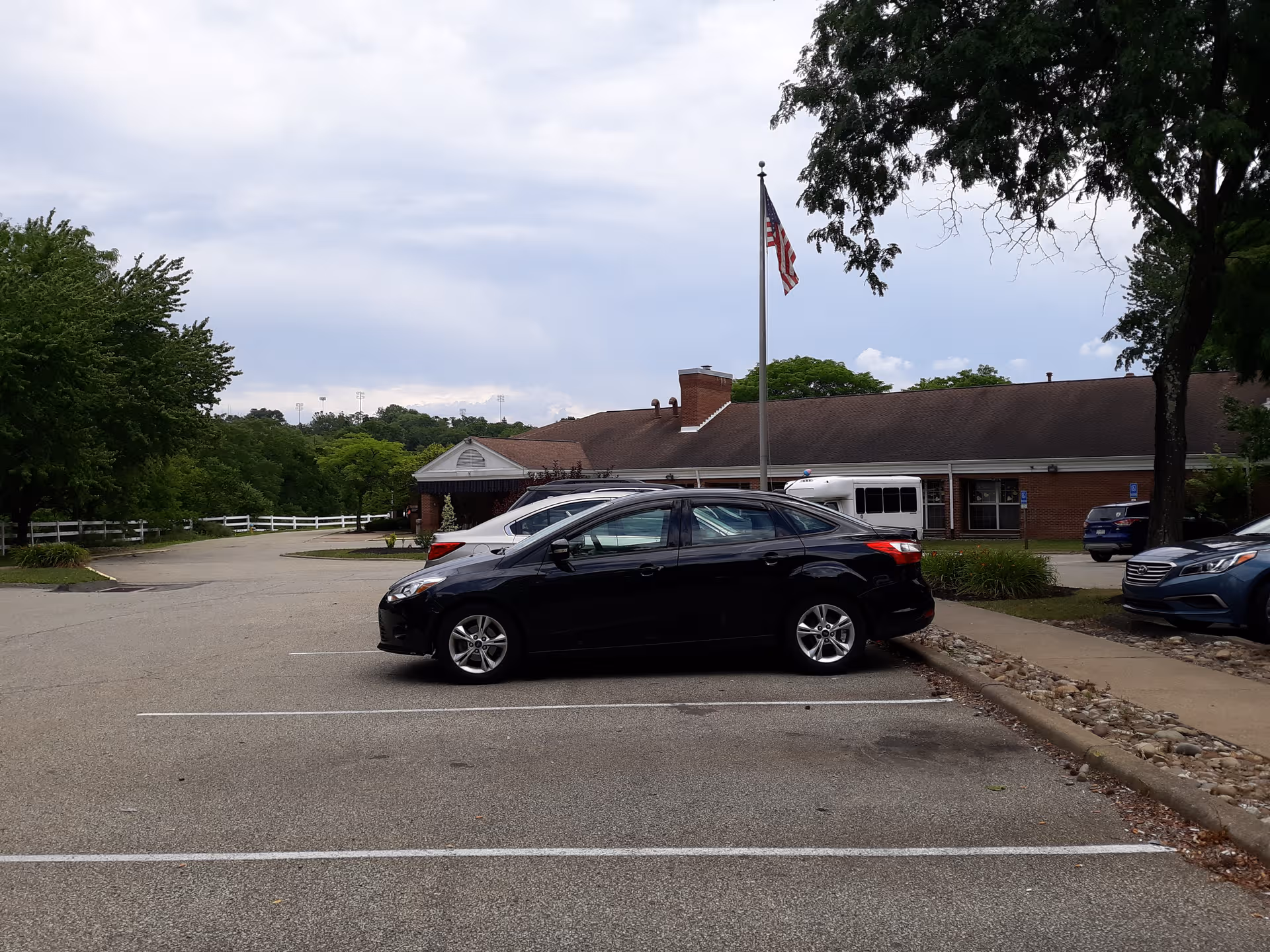 Parking lot in front of WeCare at Monroeville facility with cars and flag.